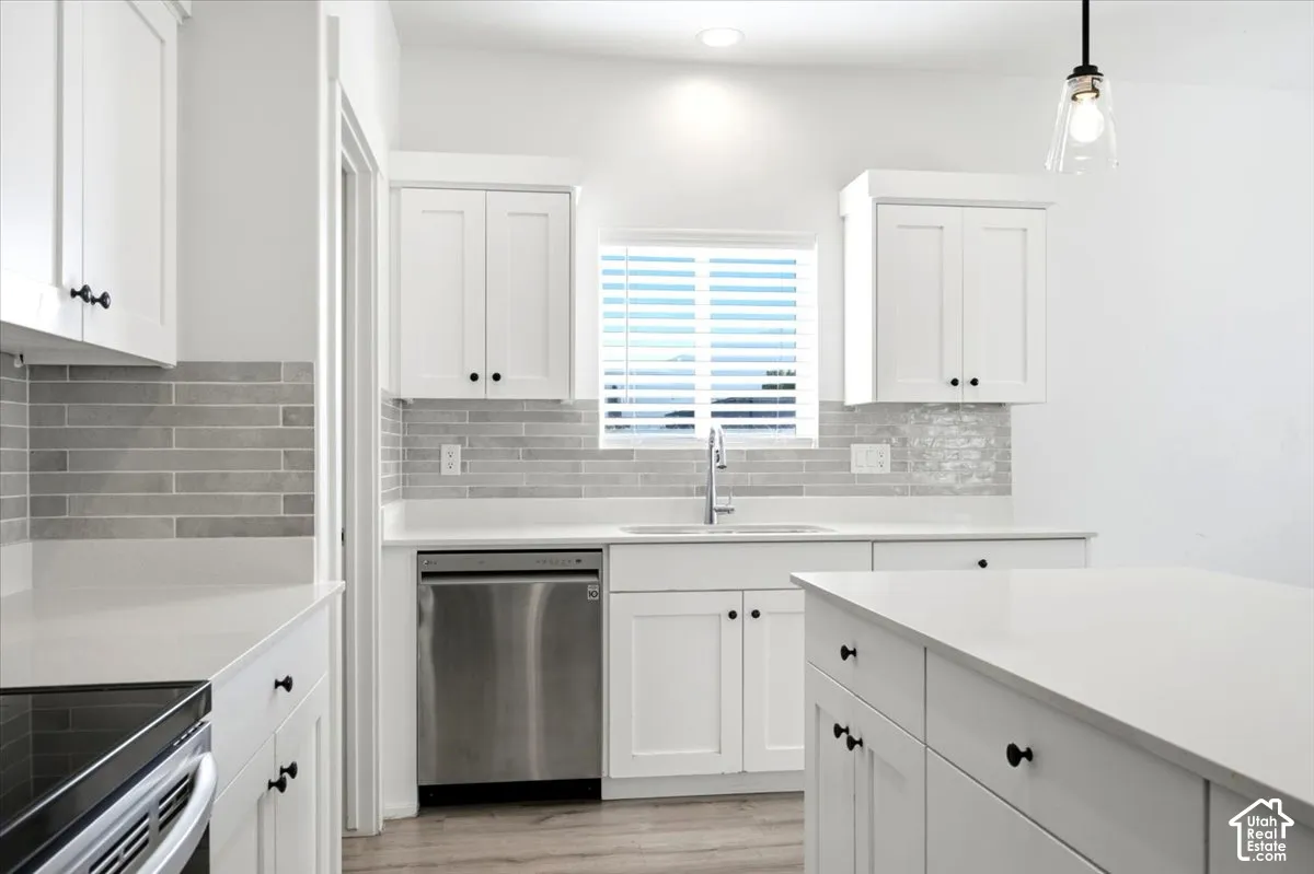 White shaker cabinetry, light-toned countertops, tile backsplash, stainless steel appliances, and a central island