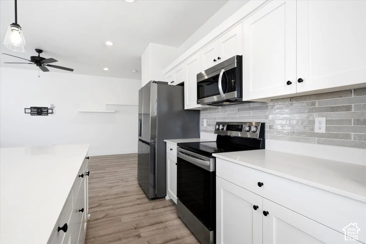White shaker cabinetry, stainless steel appliances, light wood-finish flooring, white countertops, and a gray tile backsplash