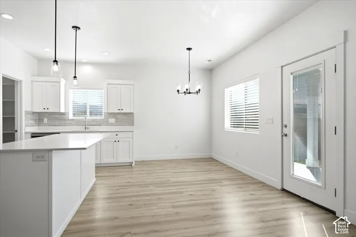 Kitchen featuring white cabinetry with dark hardware, a white island with an integrated sink, and wood-finish flooring