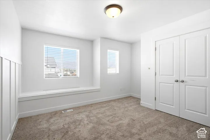 Built-in window bench, dual windows with blinds, plush carpeting, double panel doors, and a flush-mount ceiling light