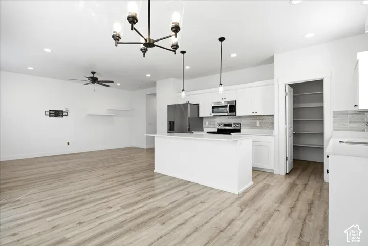 Open-concept living space featuring wood-finish flooring, a contemporary kitchen island with a white countertop, and white cabinetry