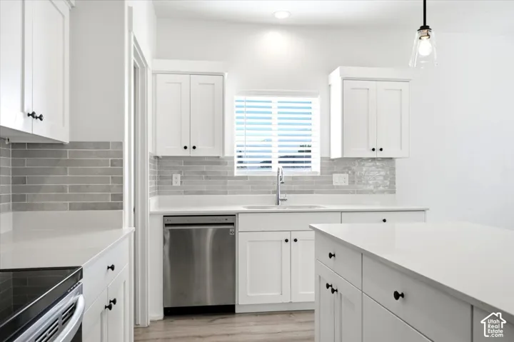 White shaker cabinetry, light-toned countertops, tile backsplash, stainless steel appliances, and a central island