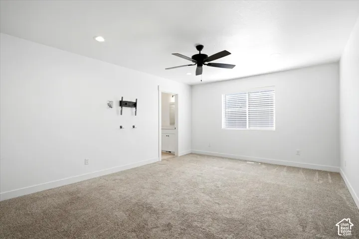Spacious bedroom with neutral carpet flooring, recessed ceiling lighting, ceiling fan with integrated light fixture, and large window with plantation shutters providing natural illumination