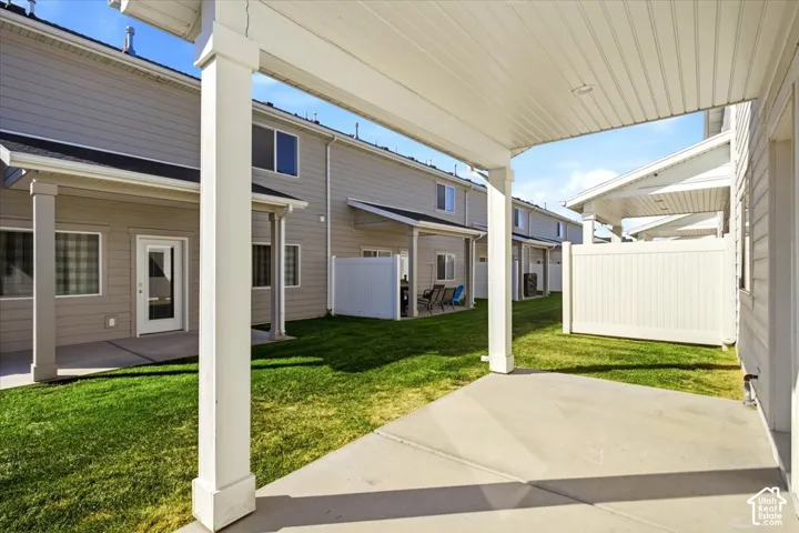 Covered patio with concrete flooring, framed by white structural columns and a white privacy fence