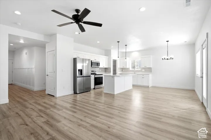 Open-concept living space with wood-finish flooring, white cabinetry, stainless steel appliances, and ceiling-mounted lighting fixtures