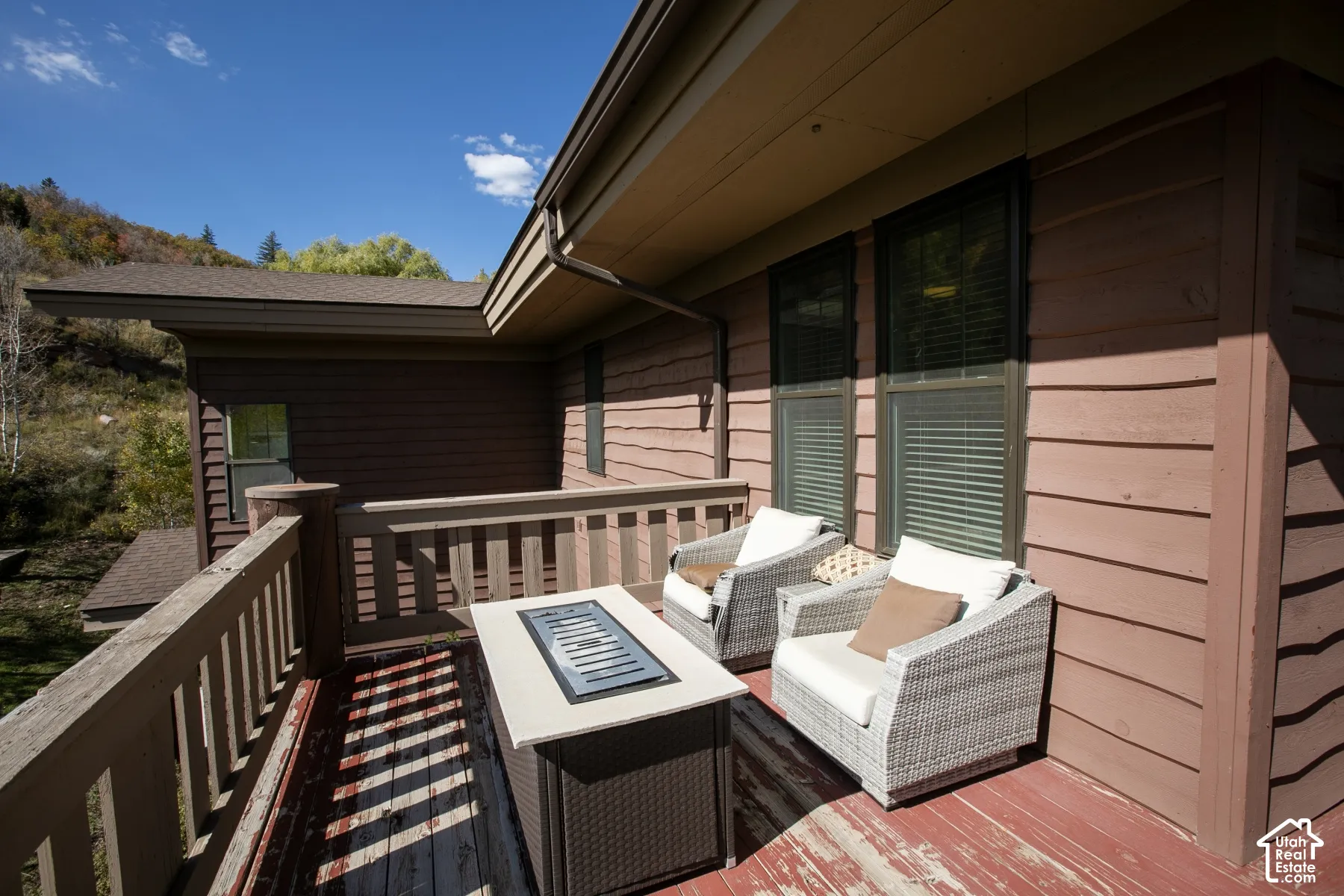 Expansive composite deck featuring multiple seating areas with woven outdoor furniture, a fire table with integrated storage, and wide composite railings