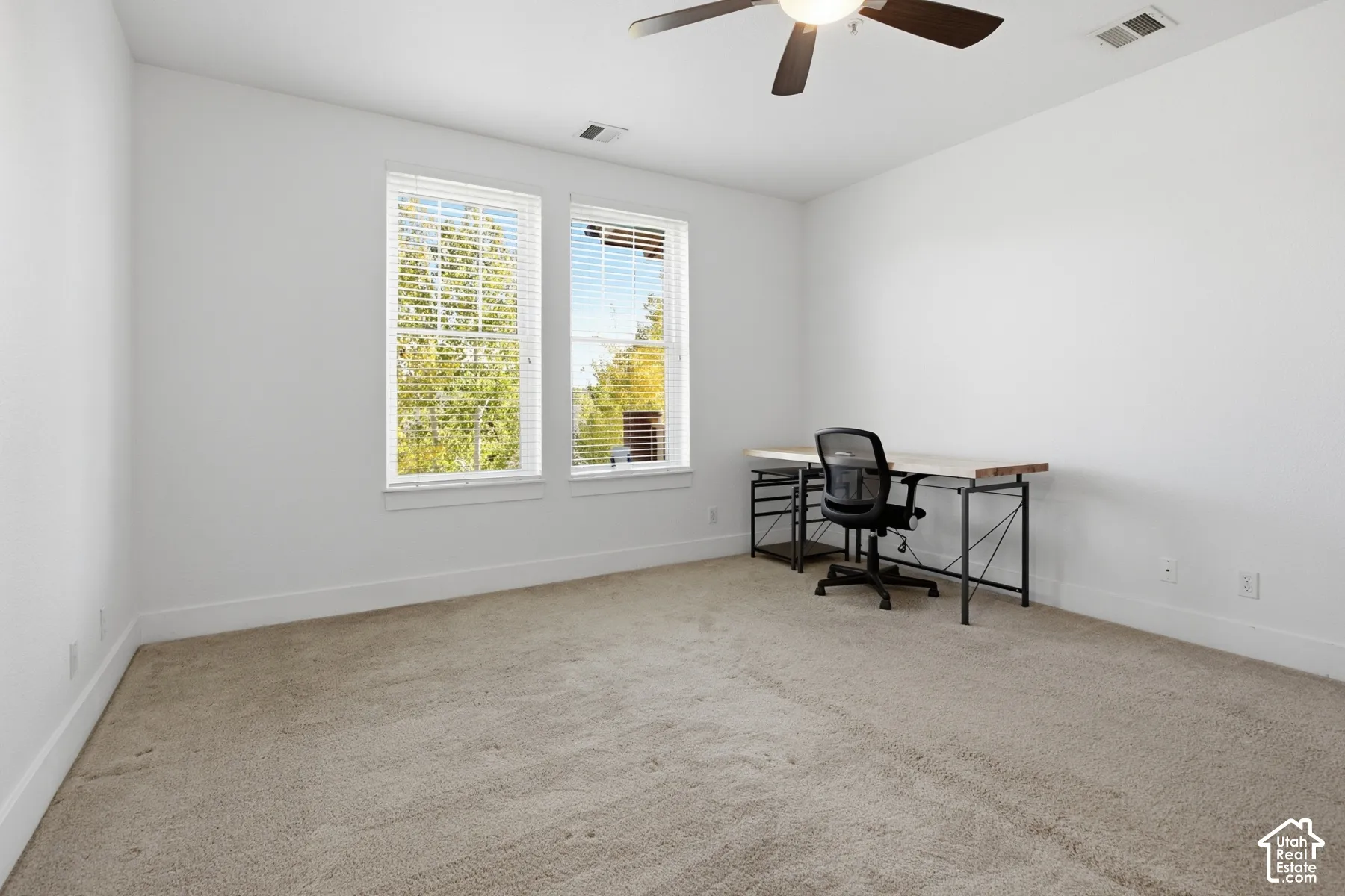 Bright room featuring two windows with blinds, neutral carpet, and a ceiling fan