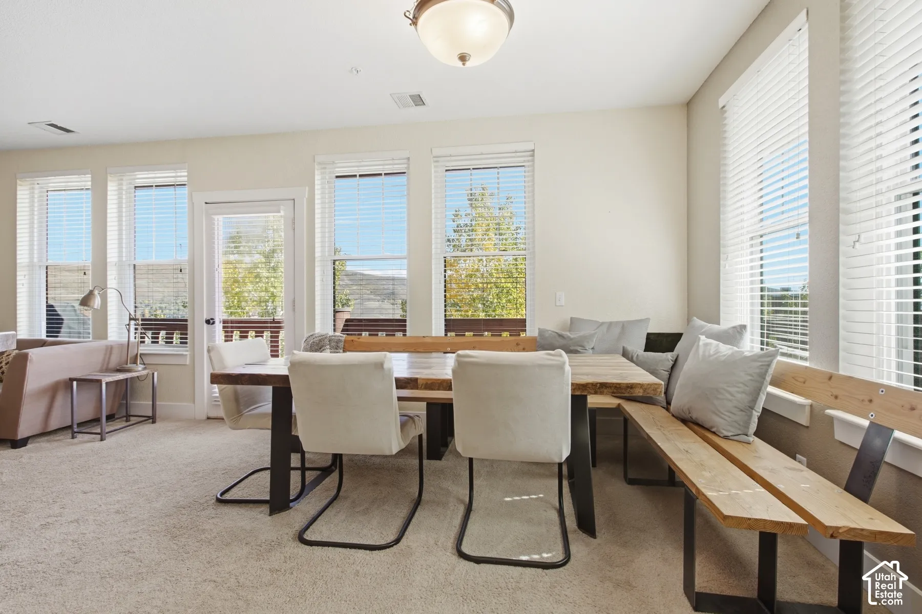 Bright dining area with multiple glass doors and windows framing scenic mountain vistas, neutral wall finishes, carpeted flooring, and a wood-finish built-in bench seating along the perimeter