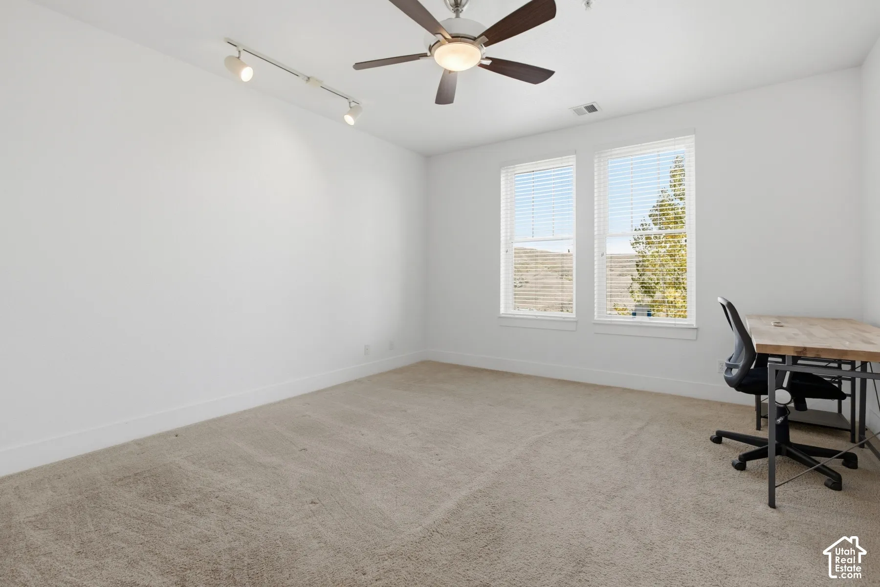 Carpeted room featuring dual windows, a ceiling fan with integrated lighting, and track lighting
