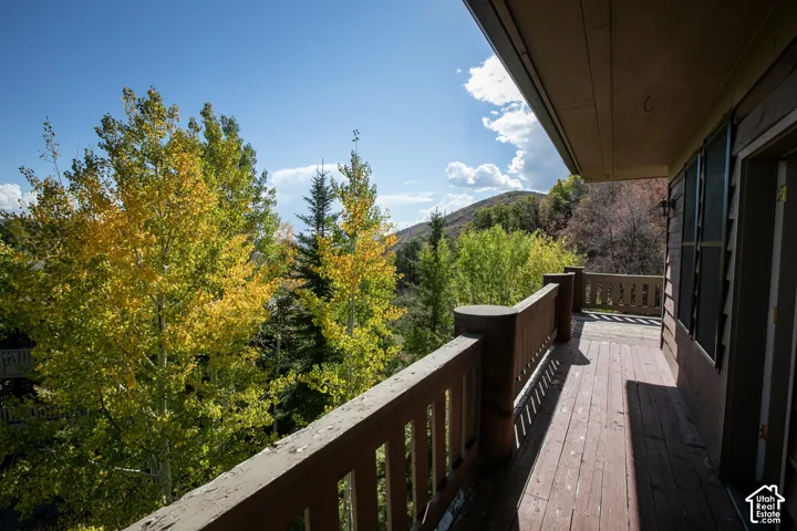 Wood deck with a substantial wood railing, framed by mature trees, under a bright blue sky