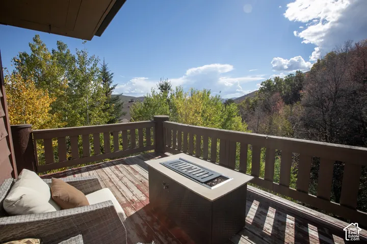 Expansive wood-plank deck with a perimeter railing and outdoor fire pit, surrounded by lush natural landscaping