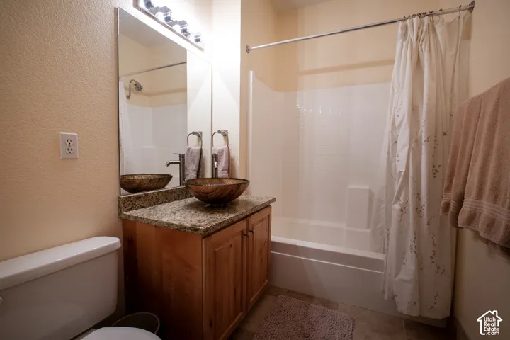 Bathroom featuring a vessel sink, wood-finish vanity with cabinet storage, granite-finish countertop, and a shower-tub combination