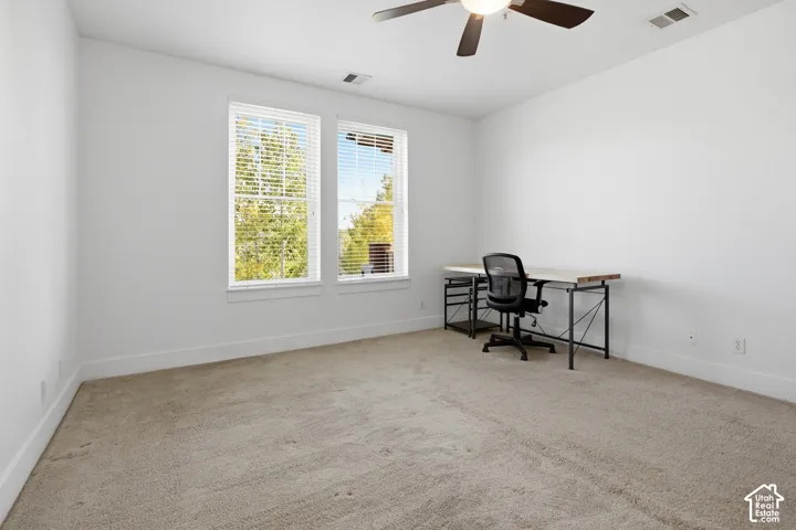 Bright room featuring two windows with blinds, neutral carpet, and a ceiling fan