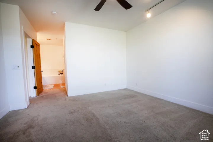 Carpeted room featuring a ceiling fan, track lighting, and a solid wood door leading to a bathroom with a built-in tub