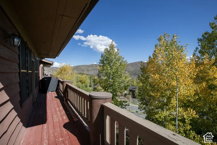Exterior deck with wood railing, shingle siding, and mature trees