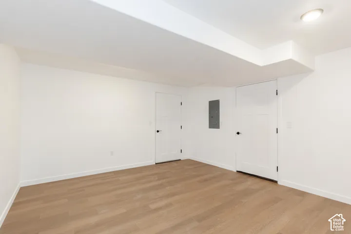 Light-toned wood-finish flooring, white walls, two interior doors with black hardware, and an overhead flush-mount light fixture