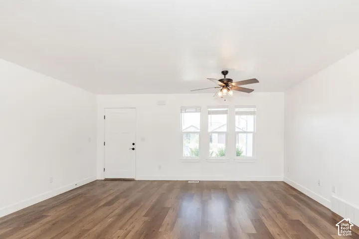 Wood-finish flooring with white trim, three windows, and a ceiling fan with integrated lighting
