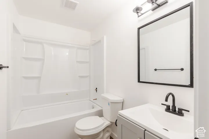 Bathroom featuring a white tub and shower surround, a toilet, a vanity with a white countertop, and a rectangular mirror with a black frame