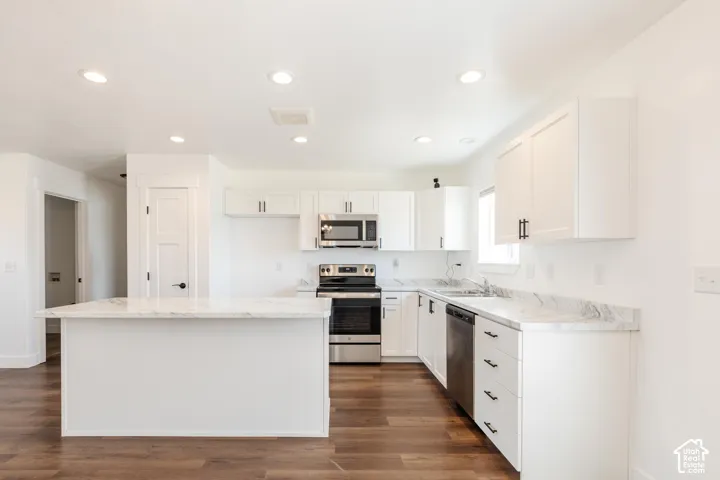 Bright kitchen featuring white cabinetry, stainless steel appliances, light-toned countertops, a central island, and wood-finish flooring