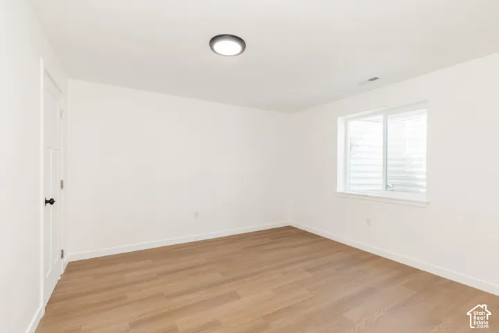 Recessed ceiling light, wood-finish flooring, white walls, white trim, and a white interior door with black hardware