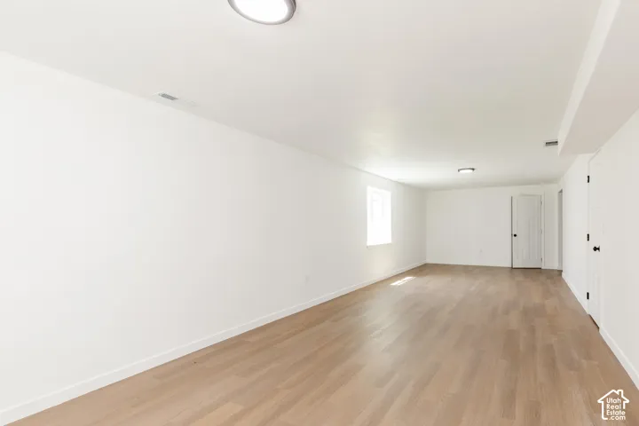 Spacious room featuring light wood-finish flooring, recessed lighting, and a white interior door with black hardware