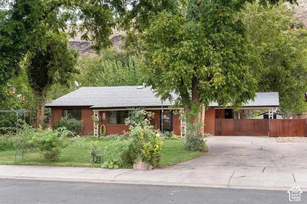 Brick exterior with a gray shingle roof, covered carport, and mature trees