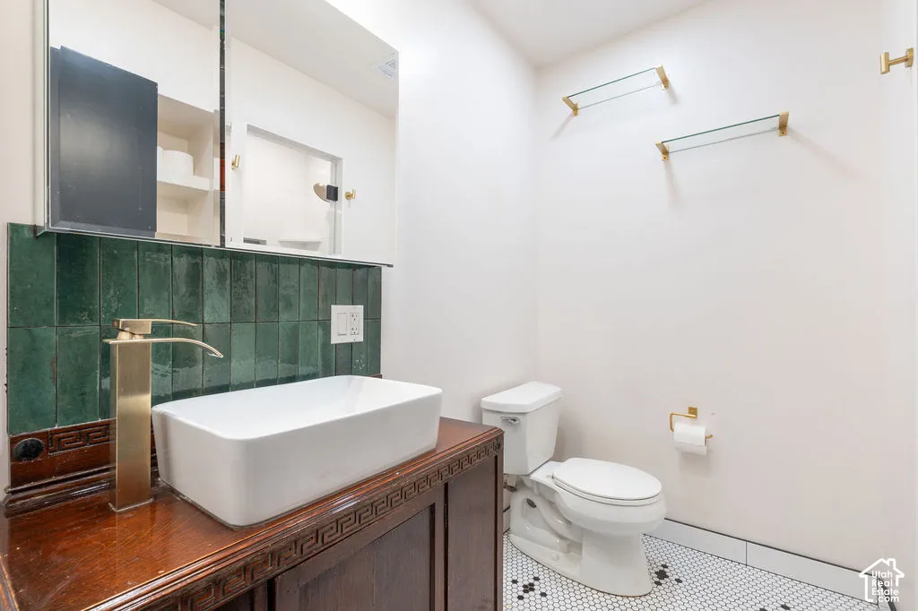 White rectangular vessel sink with a gold-finish faucet, dark wood vanity, green tiled backsplash, and mosaic floor tile