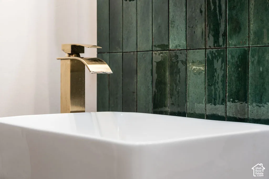 Modern bathroom featuring a sculptural brass vessel faucet with waterfall spout, crisp white rectangular basin, and a striking green subway tile accent wall with a matte finish