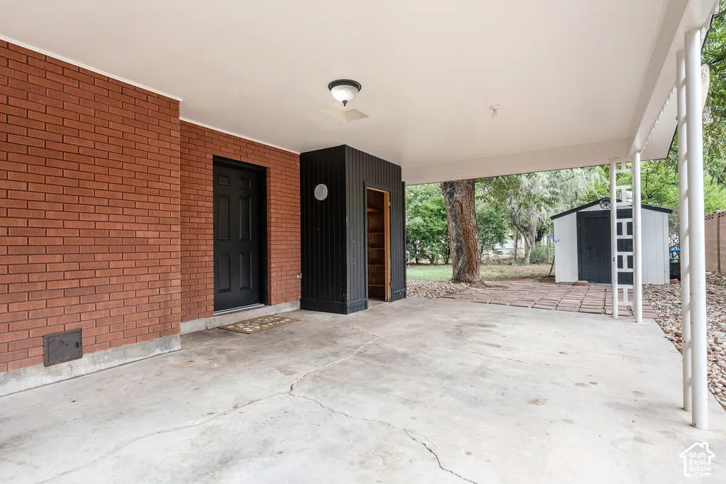 Covered patio with brick wall, black paneled door, and a storage shed