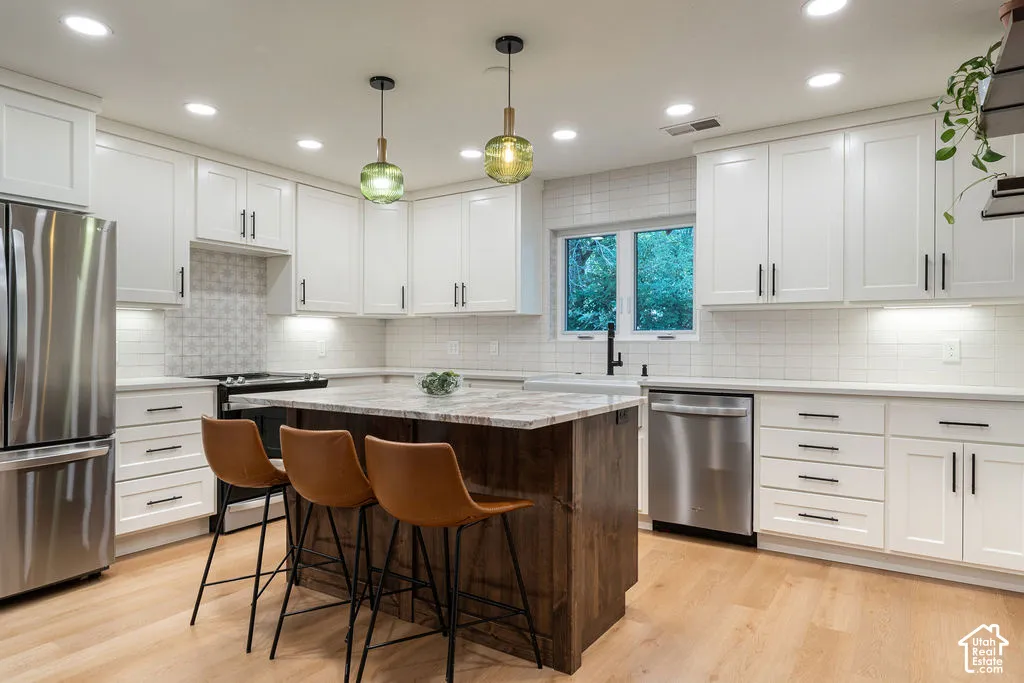 White shaker cabinetry with dark hardware, stainless steel appliances, wood-finish flooring, central island with seating, and window above the sink