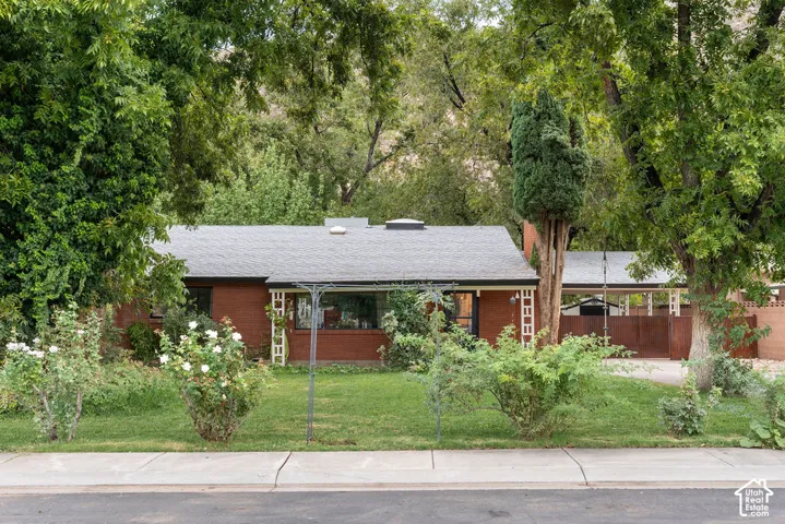 Brick ranch home featuring a gabled roofline with updated gray asphalt shingles, large window openings, and a covered front entry