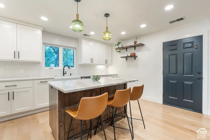 White shaker cabinetry, light wood-finish flooring, central island with stone countertop, subway tile backsplash, and recessed lighting