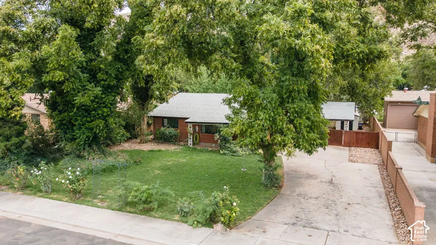 Mature trees providing natural shade, manicured lawn, paved driveway, brick facade, and a covered front entry