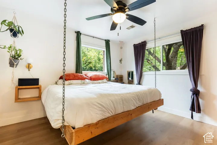 Wood-finish flooring, ceiling fan, multiple windows with natural light, wall-mounted light fixture, and floating wood shelf