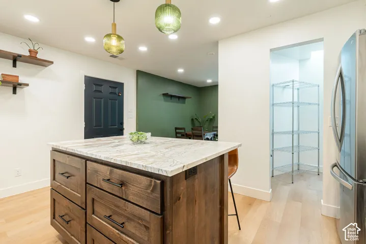 Kitchen island with stone countertop, wood-finish cabinetry, and pendant lighting