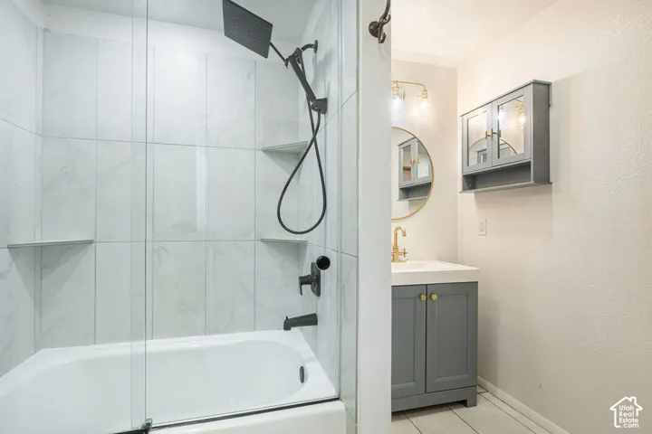 Bathtub with glass enclosure and tiled surround, featuring integrated shelving and a matte black shower system