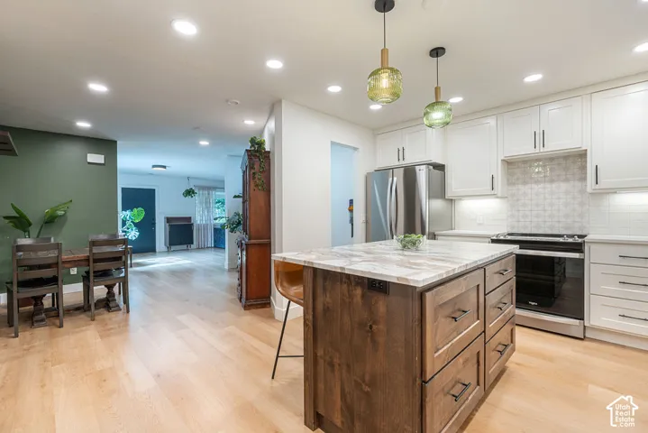 Open-concept kitchen featuring an island with stone countertop, stainless steel appliances, white cabinetry, and wood-finish flooring