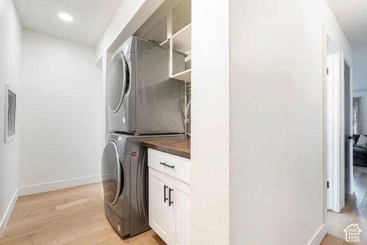 Stacked washer and dryer, white cabinetry with matte black hardware, wood-finish countertop, and recessed ceiling lighting