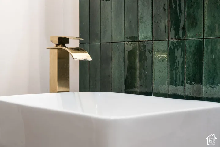 Modern bathroom featuring a sculptural brass vessel faucet with waterfall spout, crisp white rectangular basin, and a striking green subway tile accent wall with a matte finish