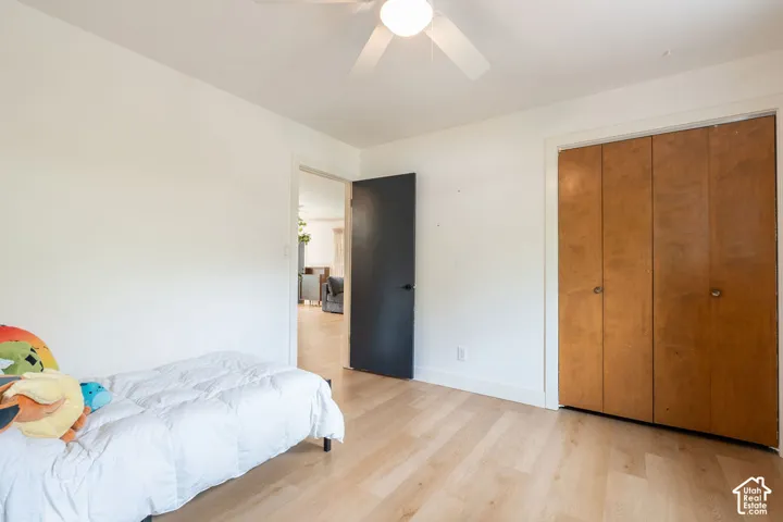 Light wood-finish flooring with white baseboards, a ceiling fan, and a light-toned closet with bi-fold doors