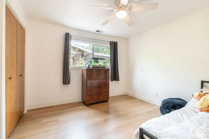 Light wood-finish flooring, a window with exterior views, a ceiling fan with integrated lighting, and a bi-fold closet with wood doors