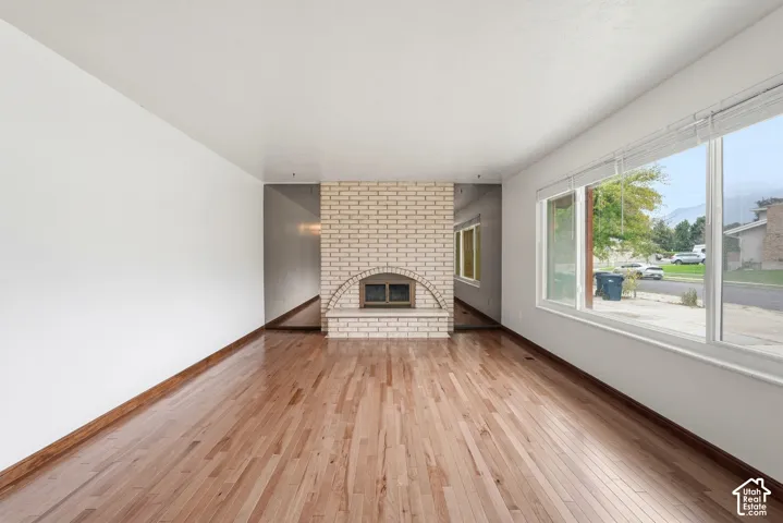 Interior space featuring wood-finish flooring, a light-colored brick fireplace with an arched firebox, a raised hearth, and large picture windows