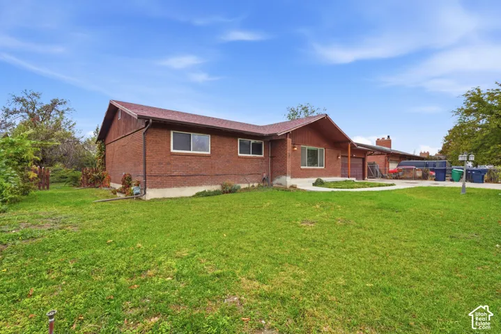 Single-story brick exterior featuring a pitched roof, attached garage, concrete driveway, and expansive lawn