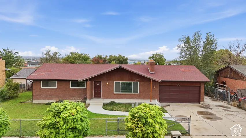 Single-story exterior featuring a brick facade, asphalt shingle roof, attached garage, and a concrete walkway