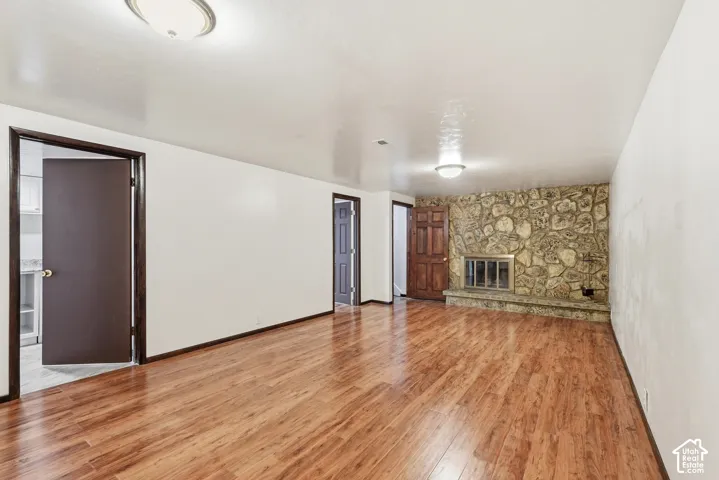 Living area featuring wood-finish flooring, a full-height natural stone fireplace with a raised stone hearth, and dark wood-stained door trim