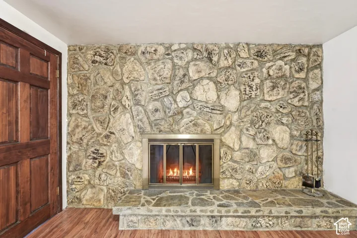 Floor-to-ceiling natural stone fireplace surround, raised stone hearth, wood-finish flooring, and six-panel solid wood door