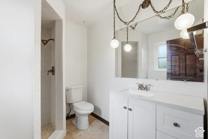 Bathroom featuring a white vanity with a solid surface countertop, tiled walk-in shower, wall-mounted chain-link light fixture, large vanity mirror, and neutral tile flooring