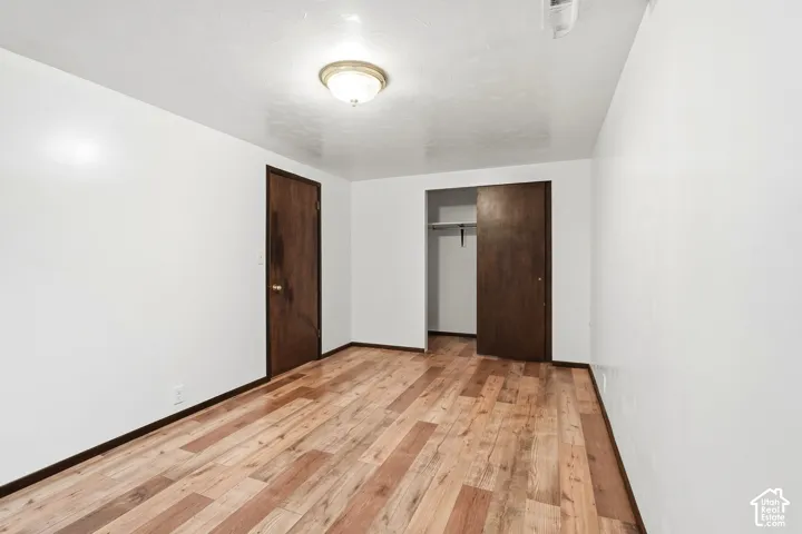 Room featuring wood-finish flooring, white walls, flush-mount ceiling lighting, a dark wood-finish interior door, and a reach-in closet with sliding dark wood-finish doors