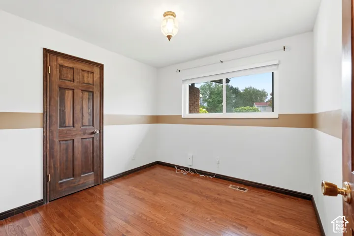 Interior room featuring wood-finish flooring, a six-panel solid wood door, and a horizontal window