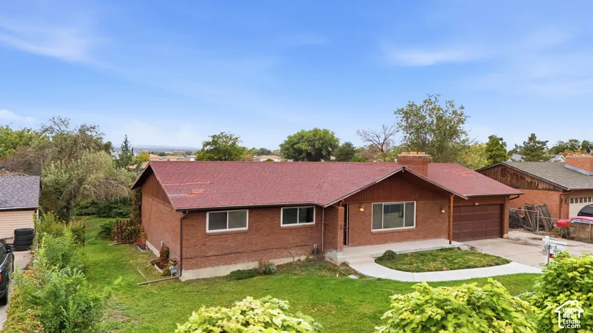 Red brick exterior featuring an asphalt shingle roof, attached garage, brick chimney, and concrete walkway